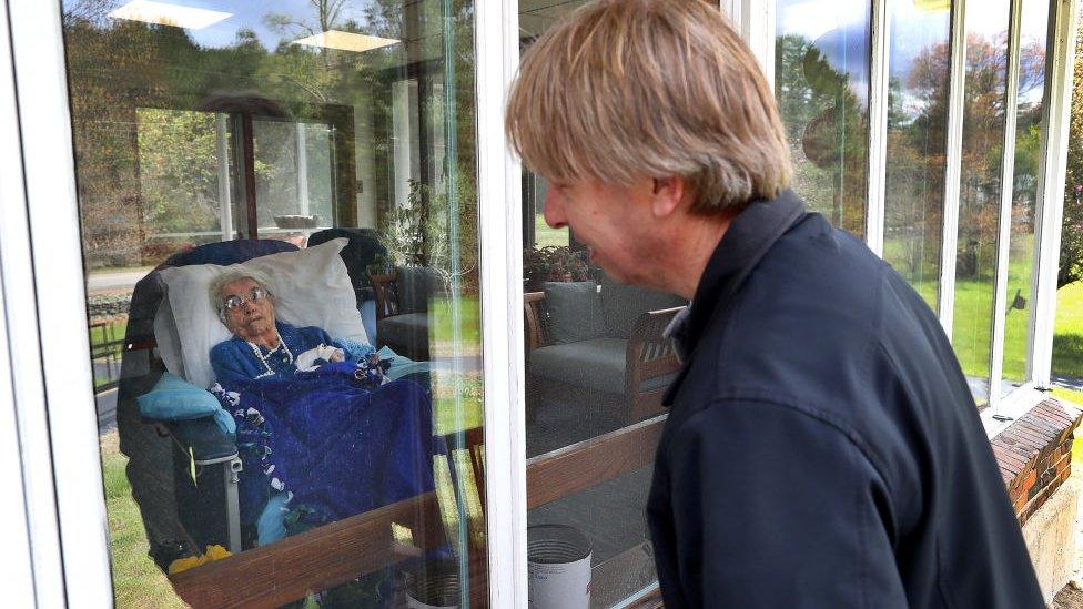 Family member looks through window at woman in nursing home