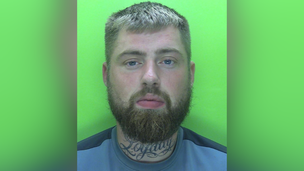 A custody photo of Luke Williamson, a white man with a large neck tattoo and a short beard with short blonde hair.