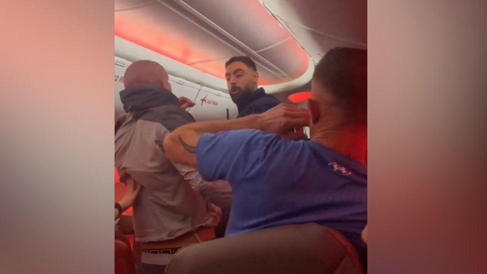 The backs of two people's heads on a plane as a police officer approaches