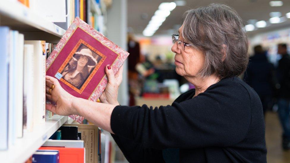 Oxfam volunteer Jacqui putting a book onto a shelf at the Wimbledon shop