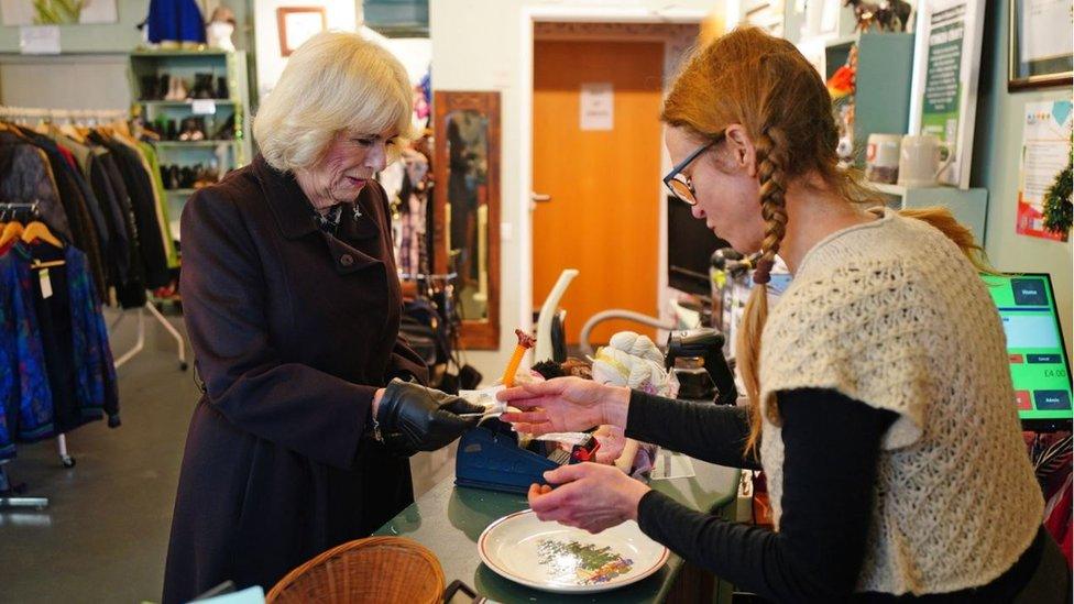 Queen Camilla buying a decorative plate over the counter at the shop