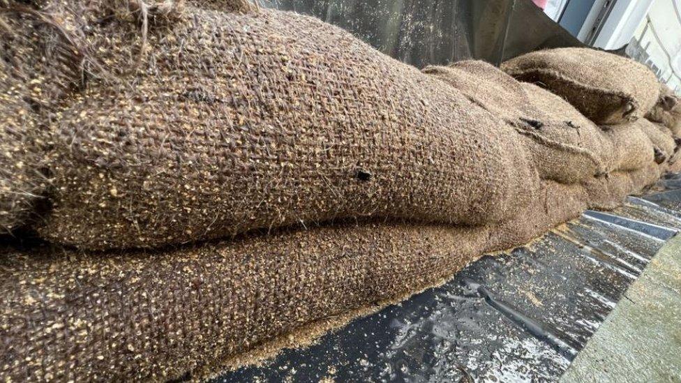 Sandbags along the edge of a house. Close-up showing them sitting on black plastic and already damp.