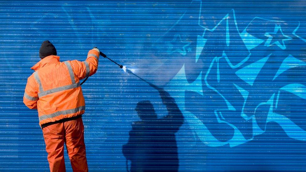 Man removes graffiti in hi vis