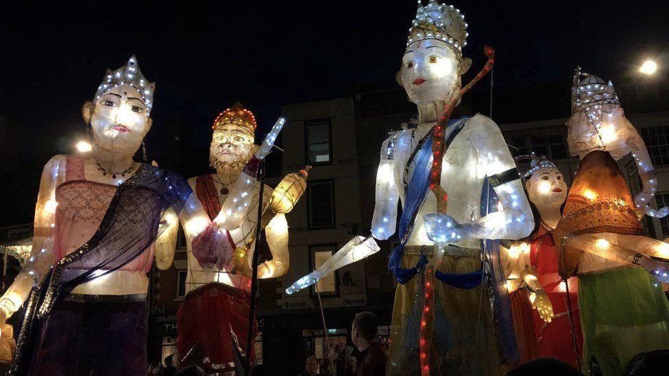 Four puppets representing people and one representing an elephant. The puppets have crowns and tiaras. They are towering above people in a parade.