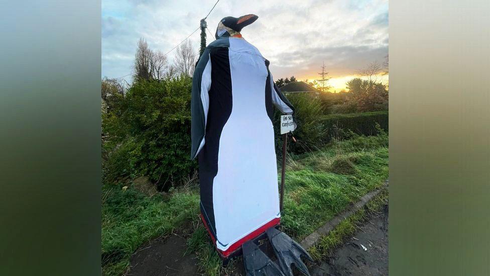 A large penguin artwork is made from black and white fabric and has an orange and black beak. It is pictured against a cloudy sky.