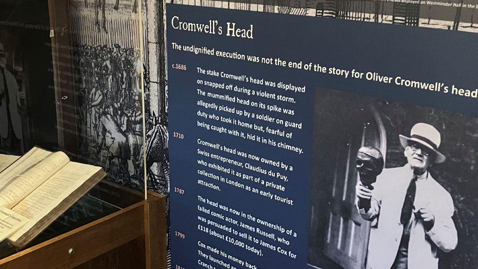 A display telling the story of Oliver Cromwell's Head in the Cromwell Museum. It lists its known whereabouts at various times in the past, and on the right is a man in a hat holding up the head