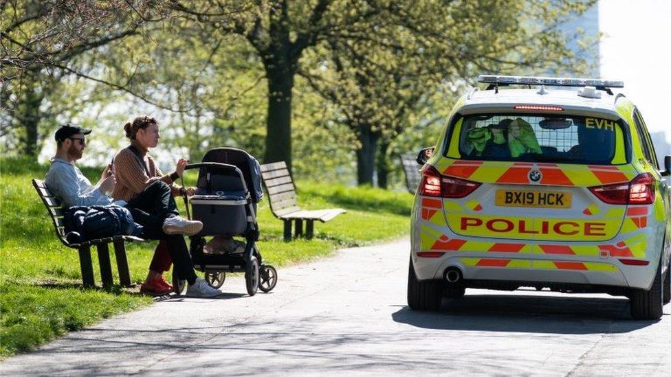 A police car near two people with a pram sat on a bench