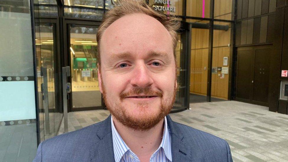 Adam Brown wearing a grey jacket outside a large office building