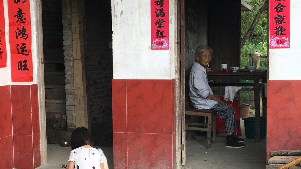 A young girl playing whilst an older lady stares out in the distance