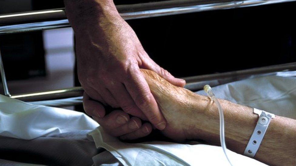 Close up of hand holding the hand of an elderly patient with an IV drip