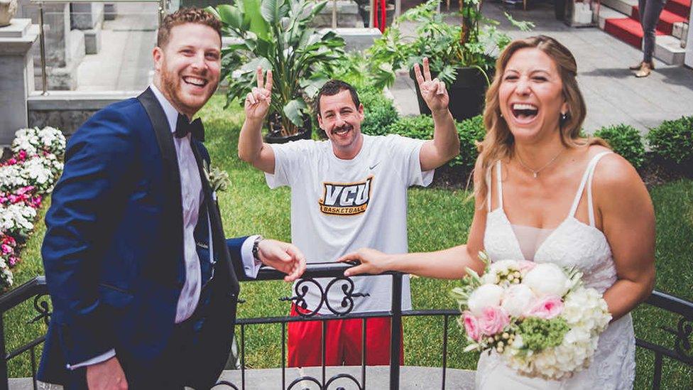 Adam Sandler dressed in running gear poses with a bride and groom at their wedding