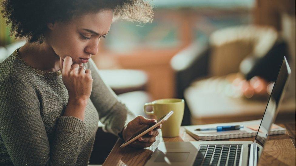 A woman holds a phone while sat at a desk