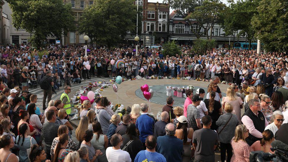 Hundreds of people gather at a vigil in Southport, holding flowers and balloons