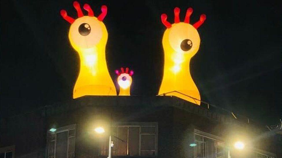 Three single yellow illuminated monster eyes on a roof with red tentacles