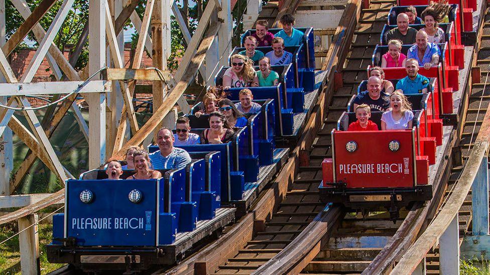 The Grand National ride on the Pleasure Beach, showing two racing rollercoasters, one blue and one red, full of smiling families.