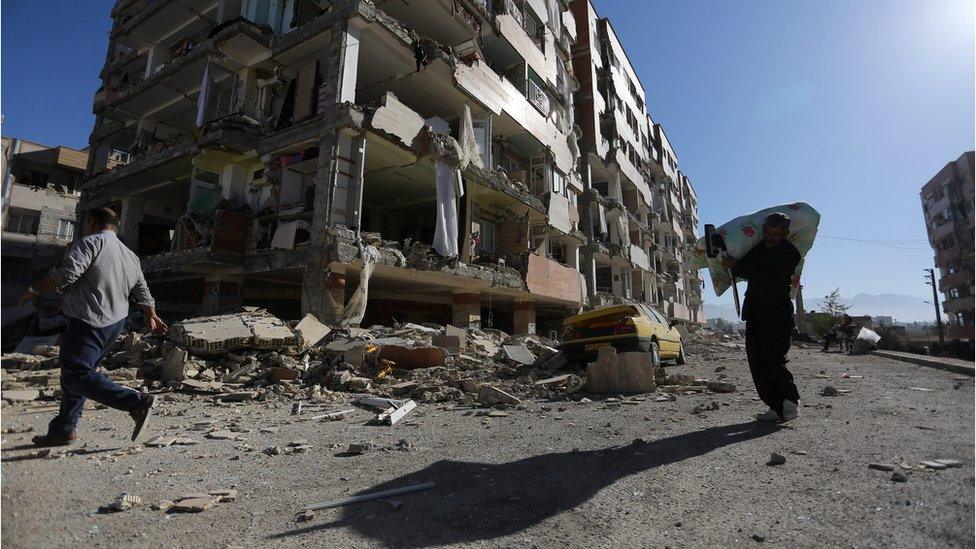 People walk past a damaged building following an earthquake in Sarpol-e Zahab county in Kermanshah, Iran November 13, 2017