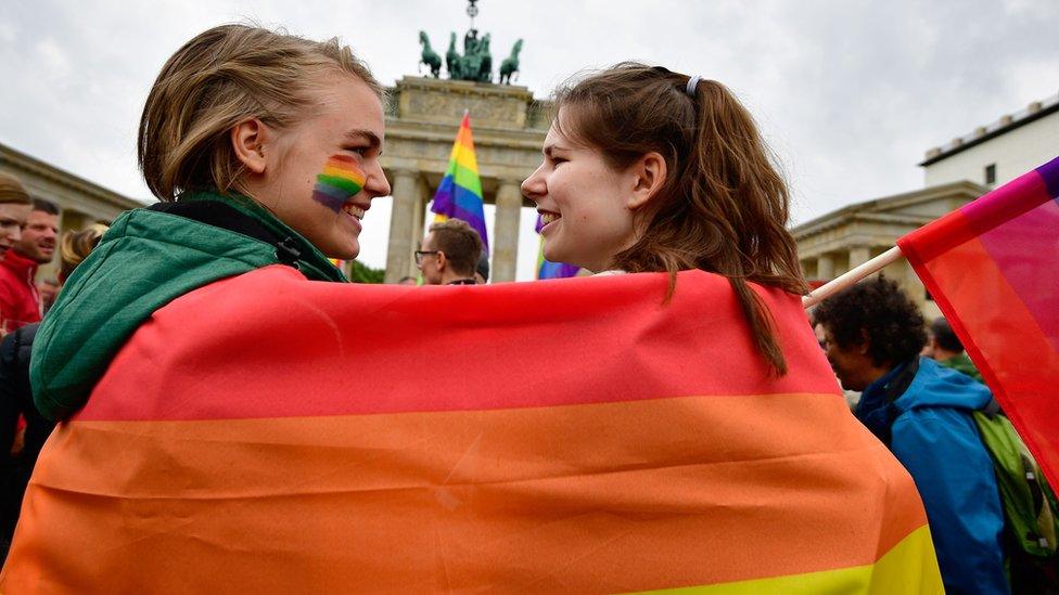 Two women wrapped in a rainbow flag at a rally in Germany