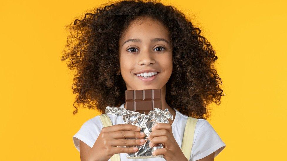 Child holding unwrapped chocolate bar.