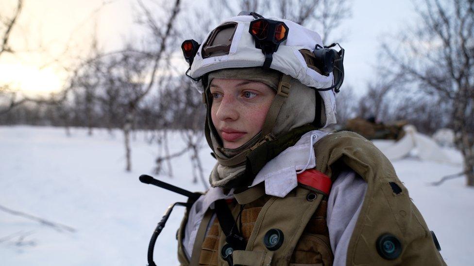 Eivor stands in uniform in the snow