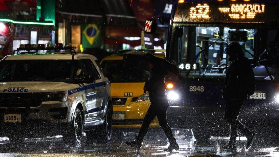 Rain pours down as pedestrians walk on a street in the Queens district of New York City, January 9, 2024.