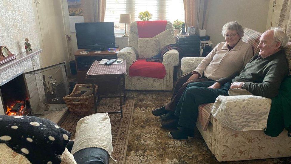 A picture showing an elderly couple Mary and Terry Laycock in front of an open fire