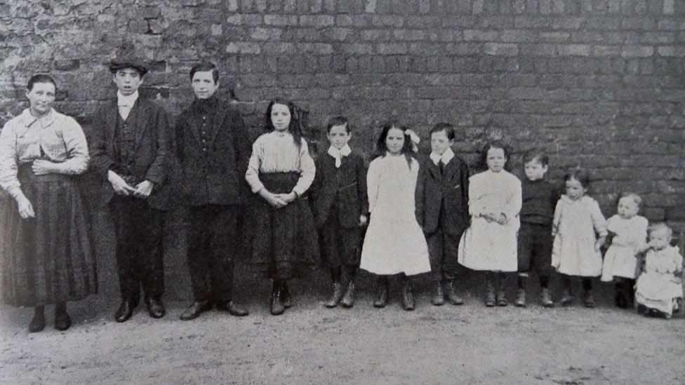 An Edwardian family showing a mother with 11 children in order of age standing against a brick wall