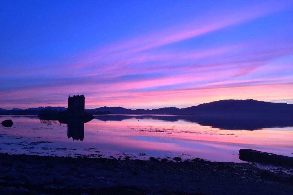 Purple sky reflected in water, also showing the silhouette of a castle.