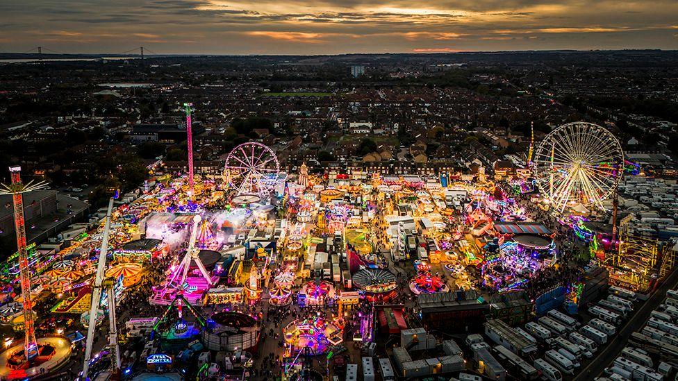 An aerial view at night showing the rides and stalls all lit up with the Humber Bridge away in the distance