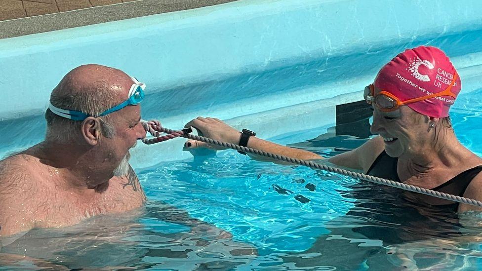 A man and a woman, both wearing swimming goggles, chat in a swimming pool