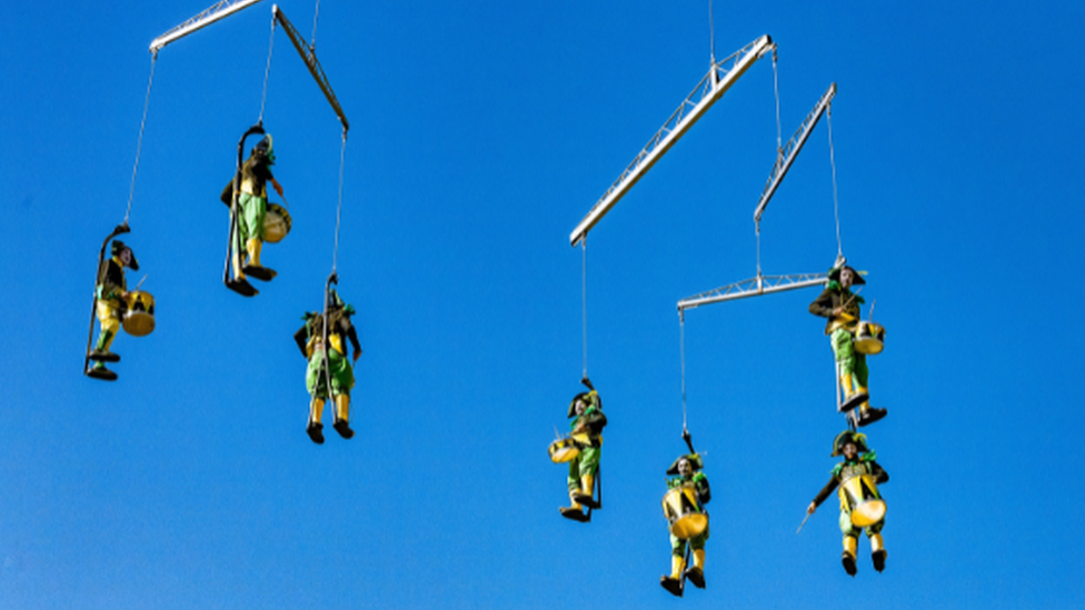 Drummers from Transe Express, suspended on a mobile hanging from a crane