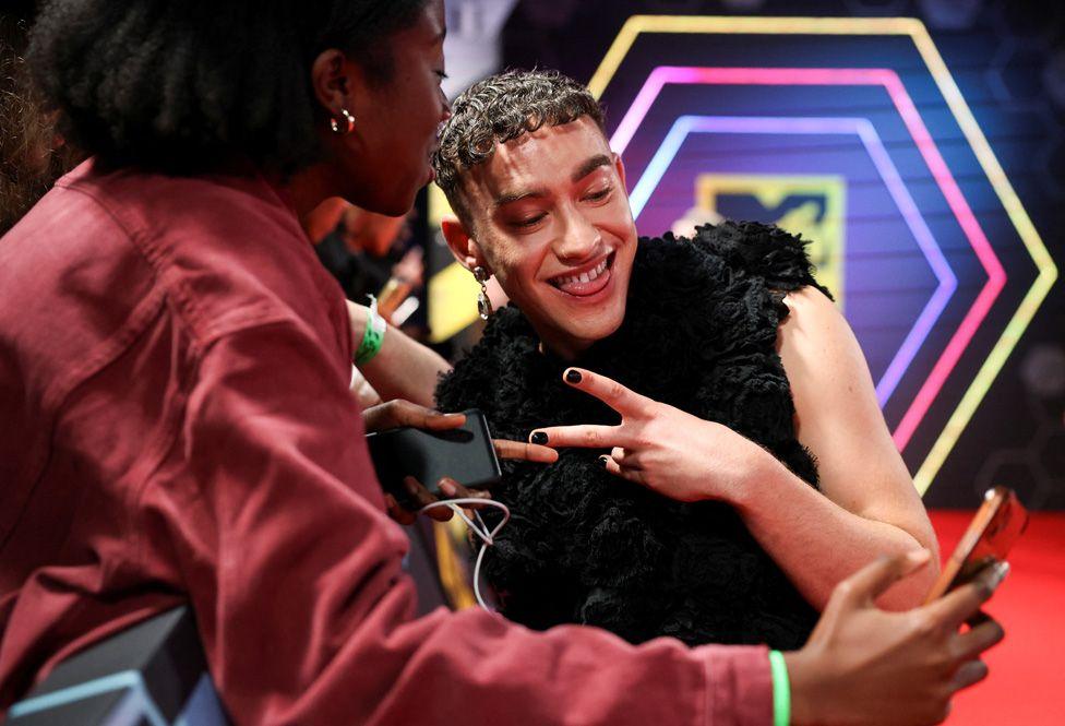 Olly Alexander posing for a selfie and flashing a peace sign with his fingers