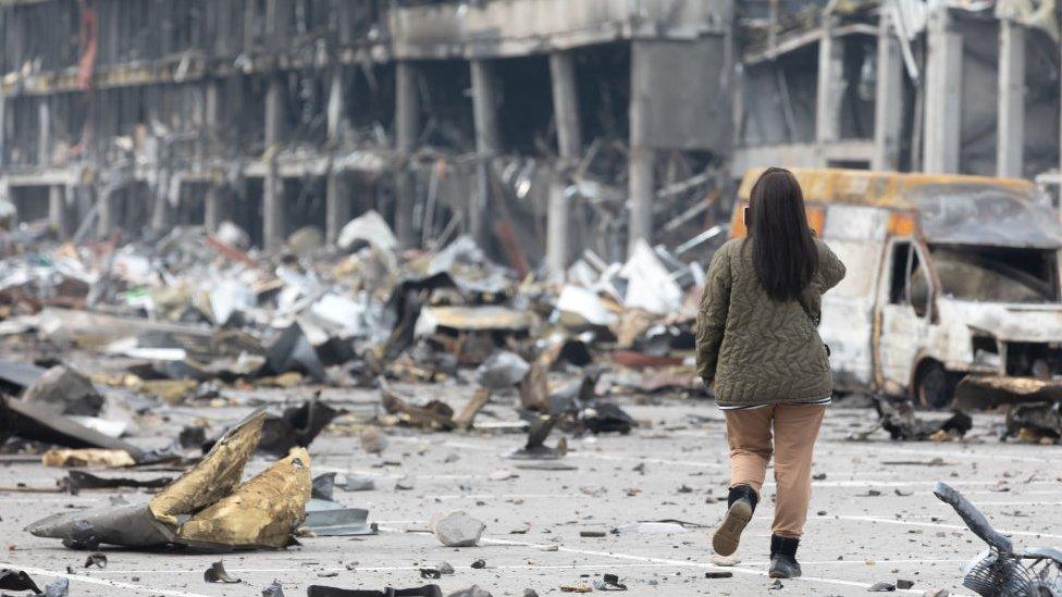 Women with mobile phone waling through war rubble.