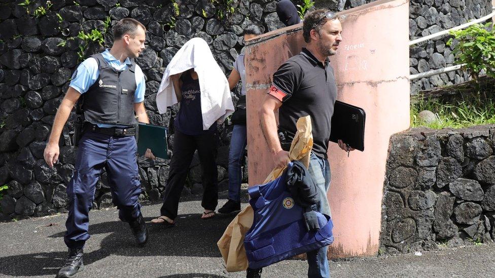 French police escort a person who is hidden under a towel