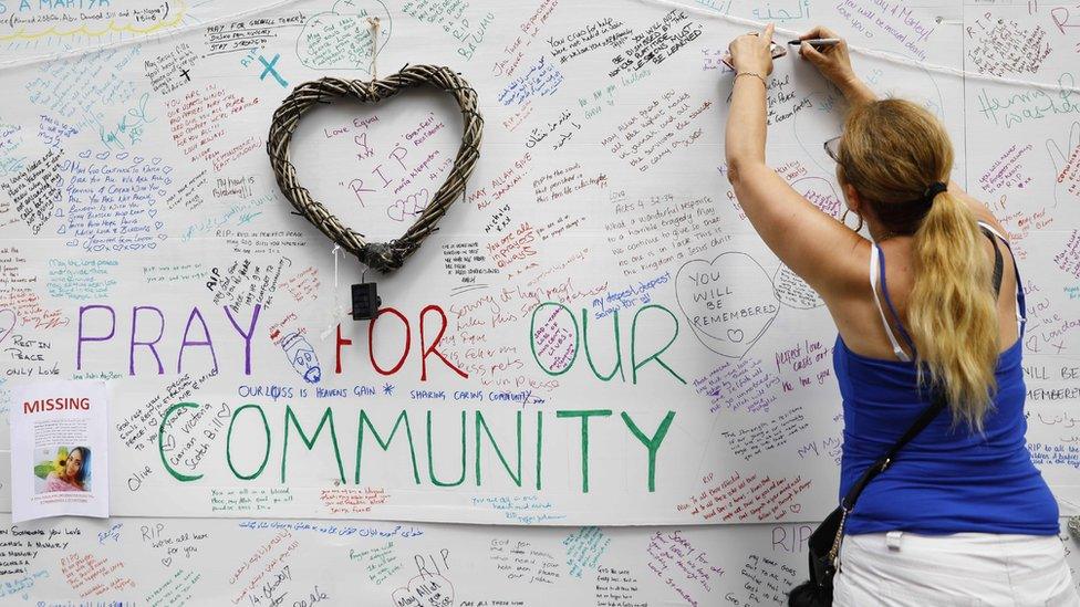 A woman writes on a message wall near to the Grenfell Tower block