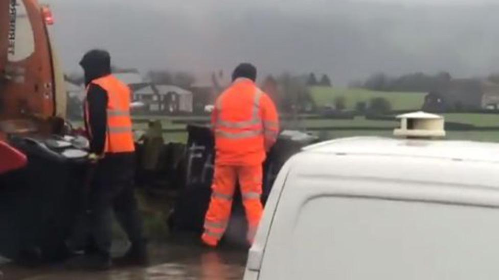 Worker appears to be urinating against dustbin