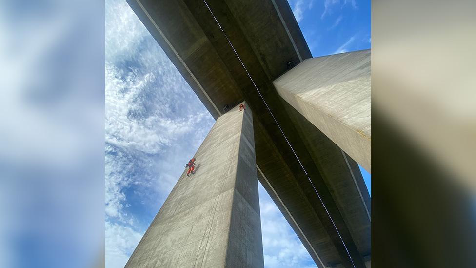 Picture looks up at the bridge close to one of the huge concrete pillars holding it up.