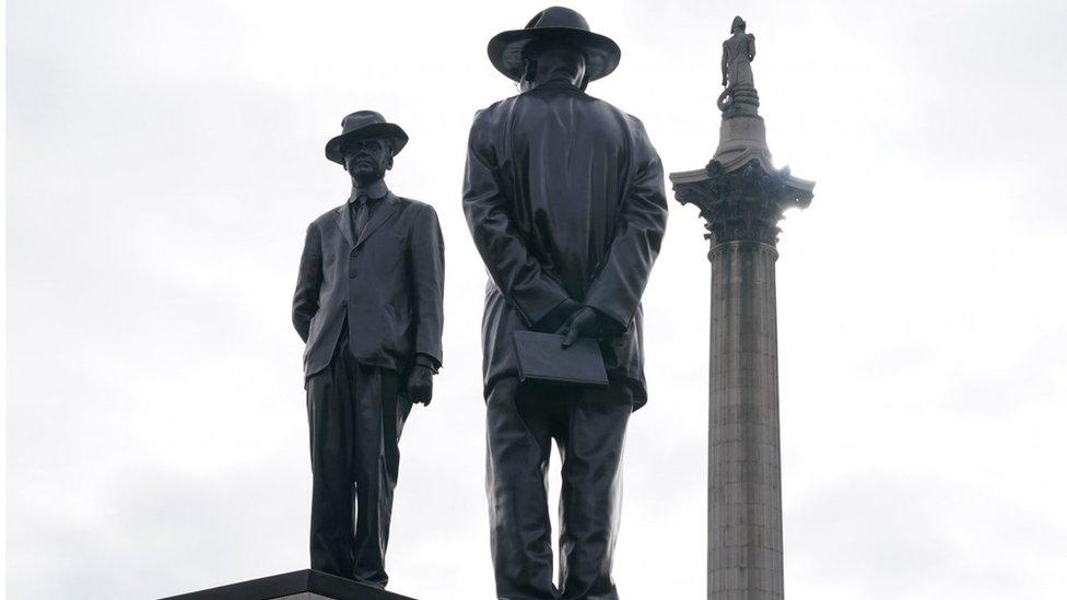 A statue at Trafalgar Square, depicting two men dressed in suits and hats