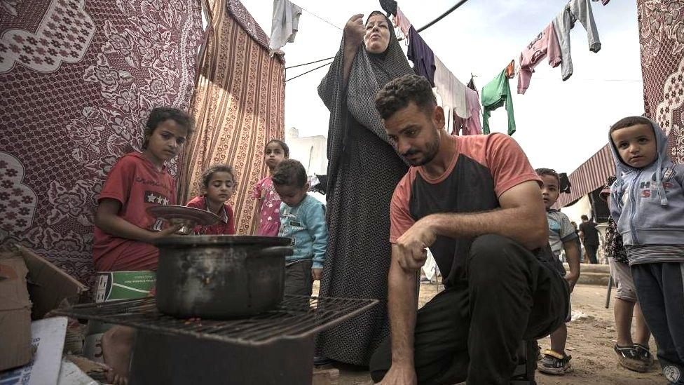 People cook food inside a tent complex in a tent camp