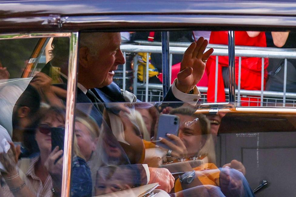 The King waves to crowds as he arrives as Buckingham palace