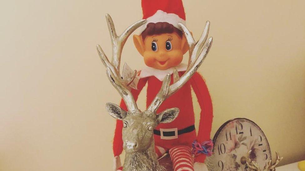 An elf wearing a red santa suit riding on a reindeer