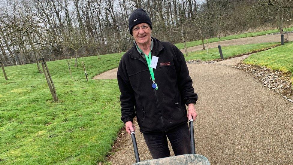 Dave Senior holding a wheelbarrow in a park area as he volunteers at Children's Hospice South West in Wraxall