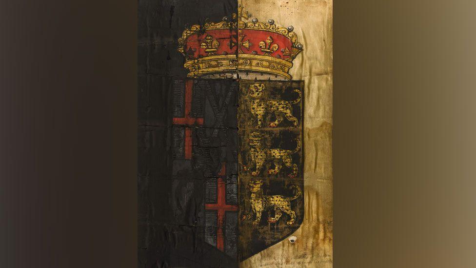 A 17th Century funeral banner from Oliver Cromwell's state funeral. It shows a shield with three leopards on the right and two red crosses on the left. Above the shield is a crown in gold and red