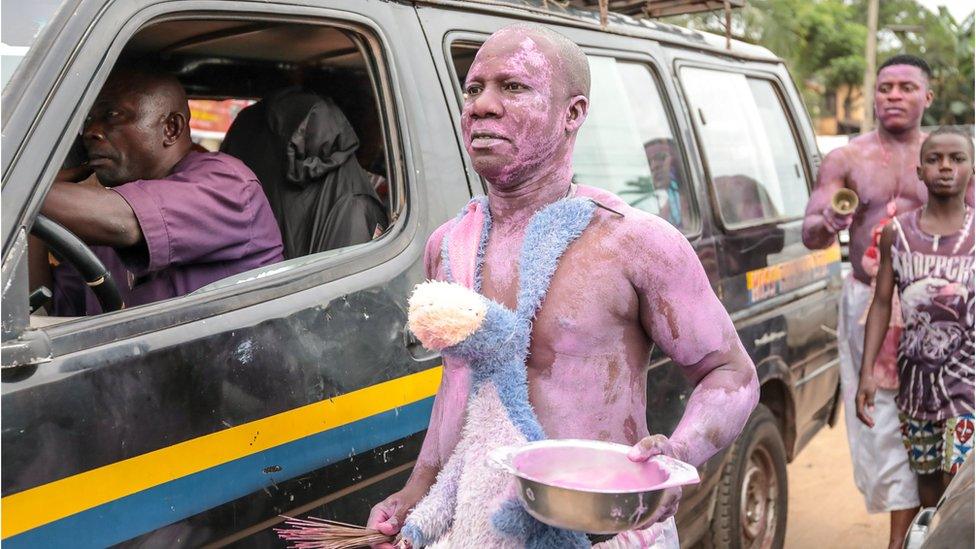 Men covered in purple paint walking next to a car in a street parade in Arondizuogu during the Ikeji Festival in Nigeria