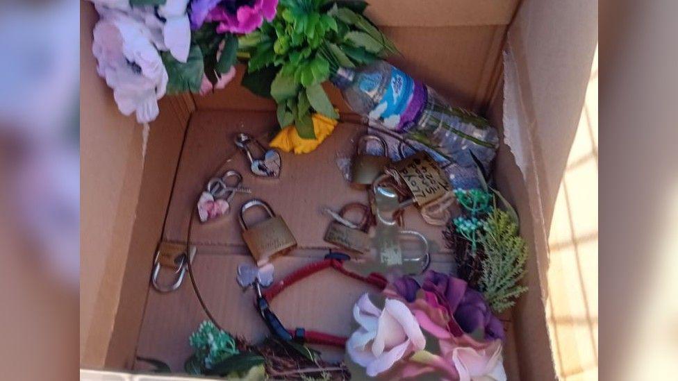 A box full of memorial items taken away from the sea wall including artificial flowers and several padlocks, some with photos of people on