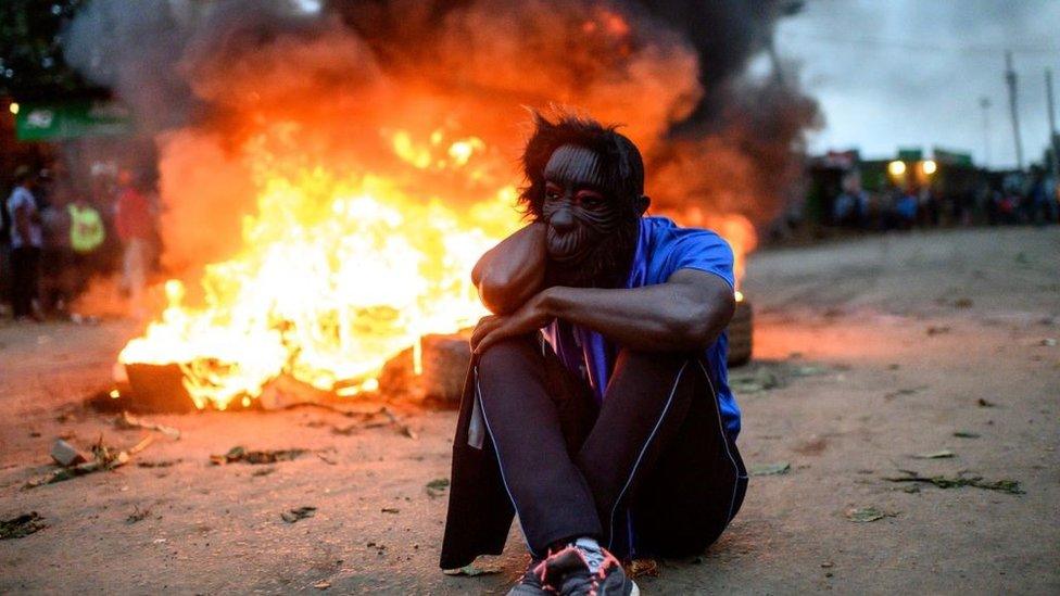 A supporter of Kenya's Azimio La Umoja Party (One Kenya Coalition Party) presidential candidate Raila Odinga reacts past burning tyres during a protest against the results of Kenya's general election in Kibera, Nairobi, western Kenya on August 15, 2022.