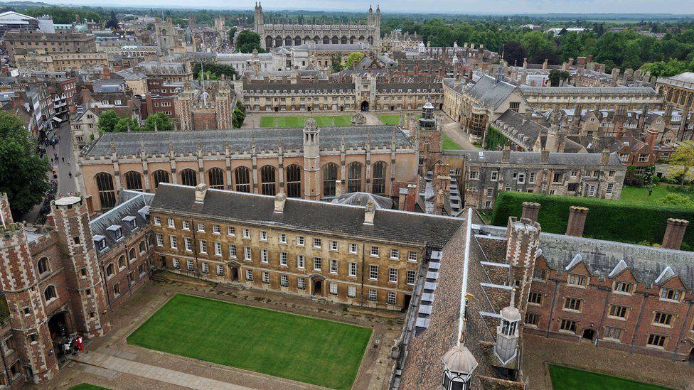 An aerial shot showing many of the University of Cambridge's colleges. The buildings are in grids around grass squares. In the distance on the right can be seen a mass of trees.