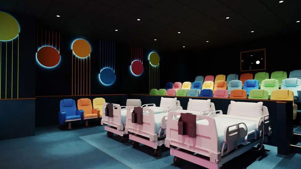 Inside the MediCinema at Alder Hey which has multicoloured seating and three hospital beds in a row at the front with extra reacting at the side