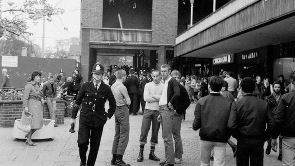 A police officer passes skin heads in Coventry
