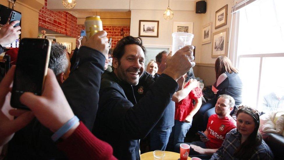 Paul Rudd raising a pint glass in the Turf pub in Wrexham before Wrexham FC's game against Boreham Wood