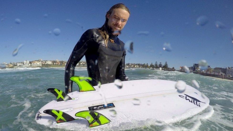 Surfer Arlen Macpherson checks the electronic shark repellent device he had installed in his board as he exits the water at Sydney's Bondi Beach (18 August 2015)